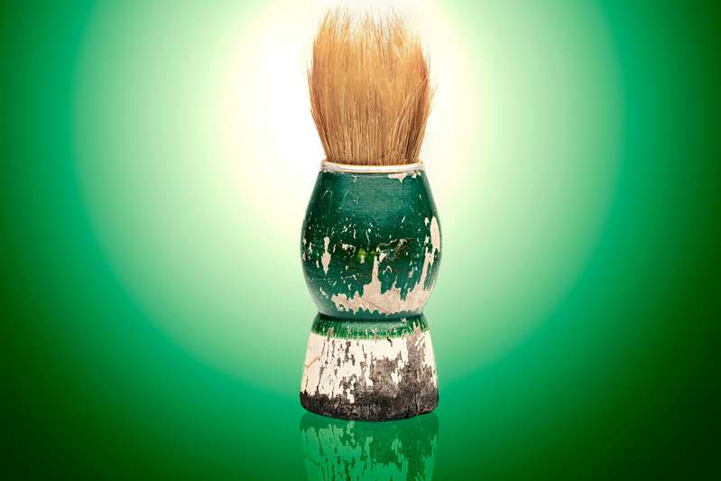 Two bearded men examining a handmade shaving brush on a wooden countertop with grooming products in the background